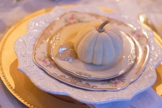Holiday table setting with gold-rimmed plates and a small white pumpkin